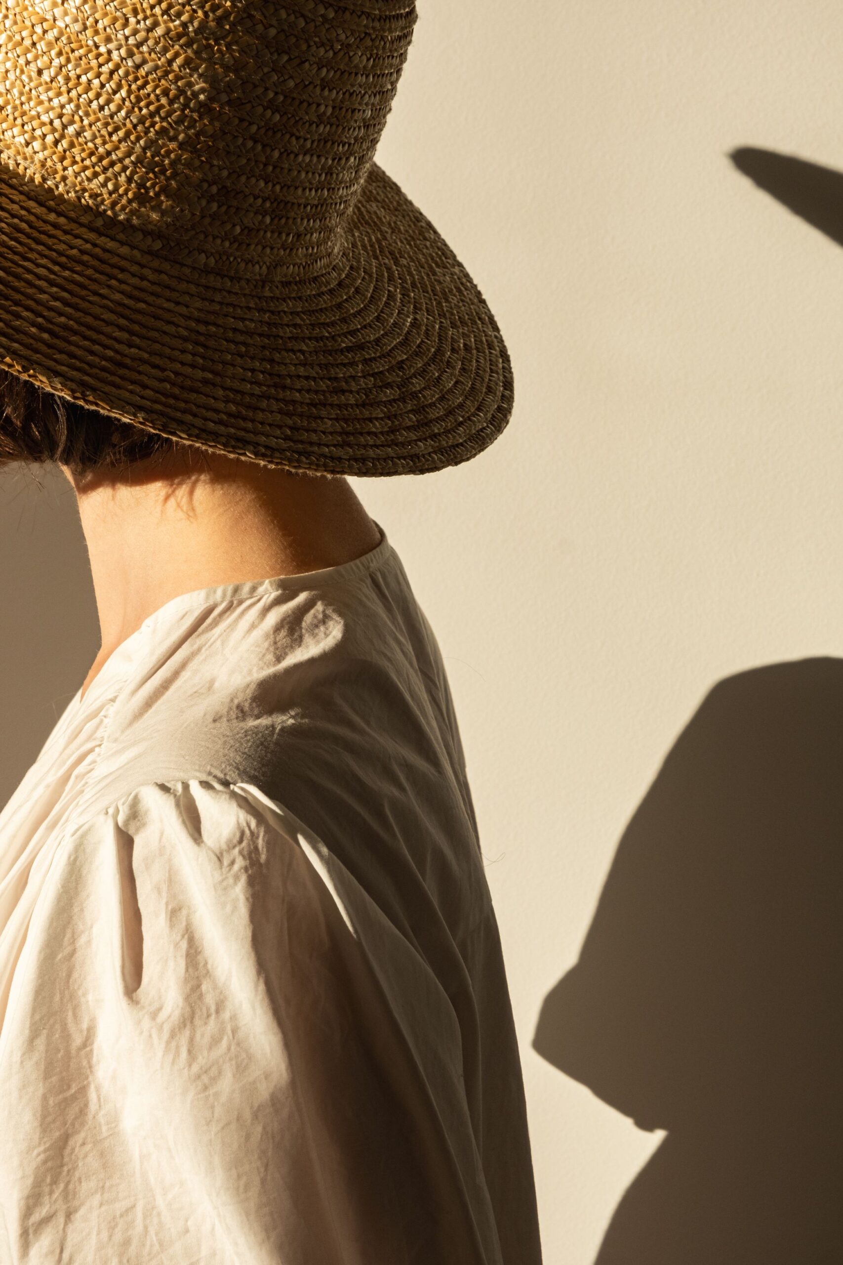 young-pretty-woman-straw-hat-white-dress-sundress-against-wall-sunlight-shadow-wall